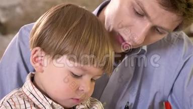 年轻的爸爸和他的小儿子在纸上写字，拿着写字板，爸爸帮助和教他的儿子写字